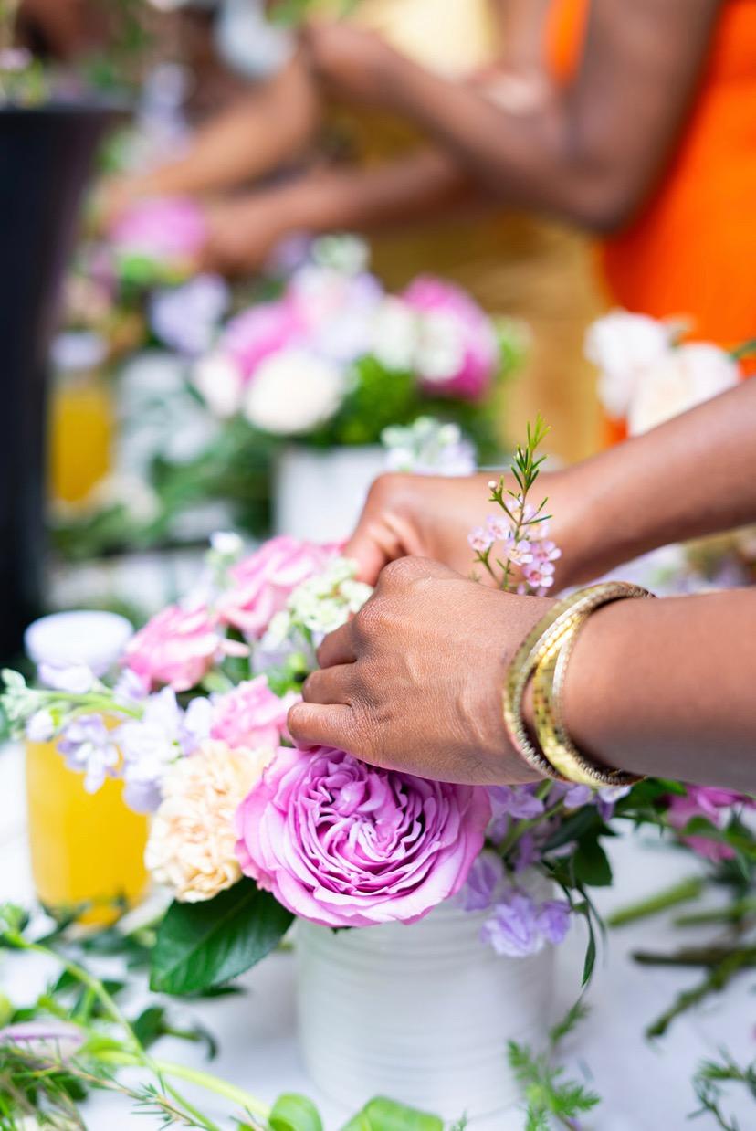 Close-up of hands delicately arranging a bouquet of purple roses and pastel flowers in a white vase, showcasing floral design skills.