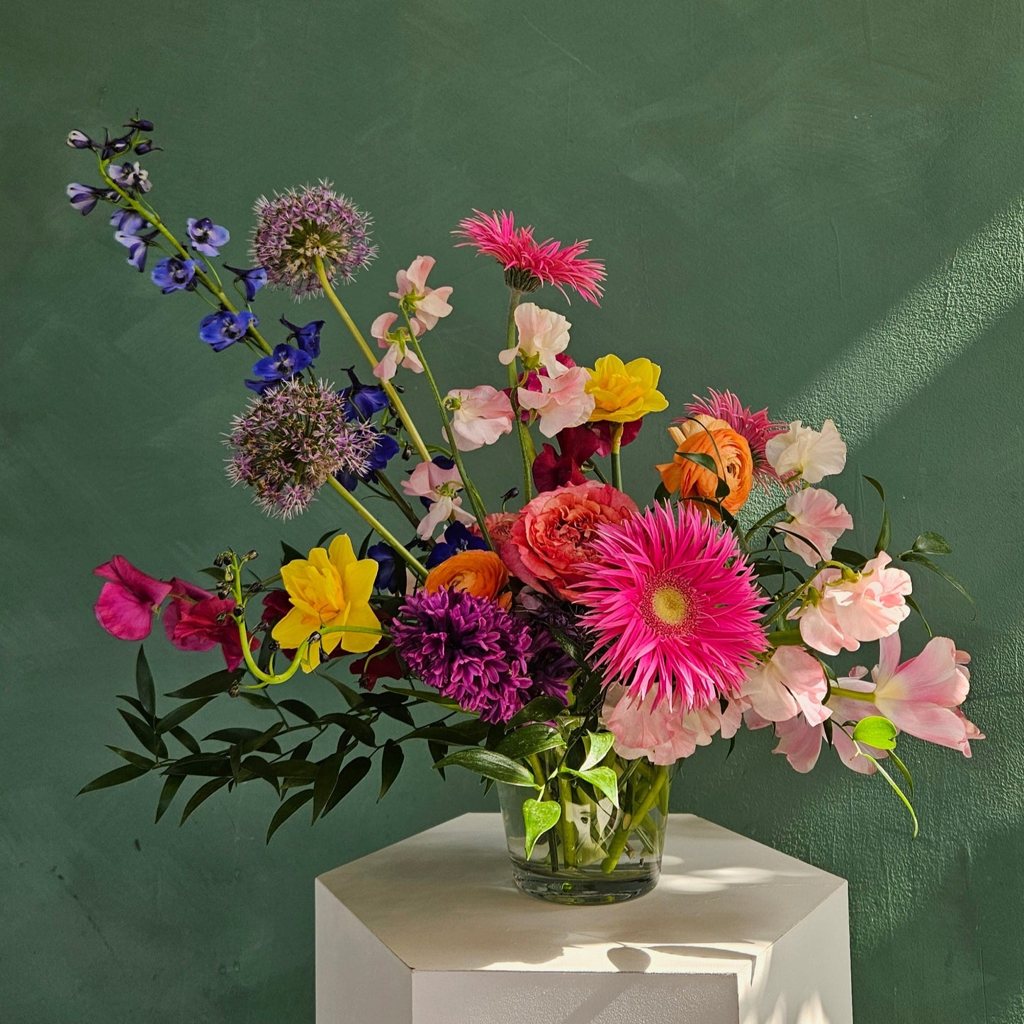 Colorful spring flowers artfully arranged is a clear glass vase, photographed against a green background