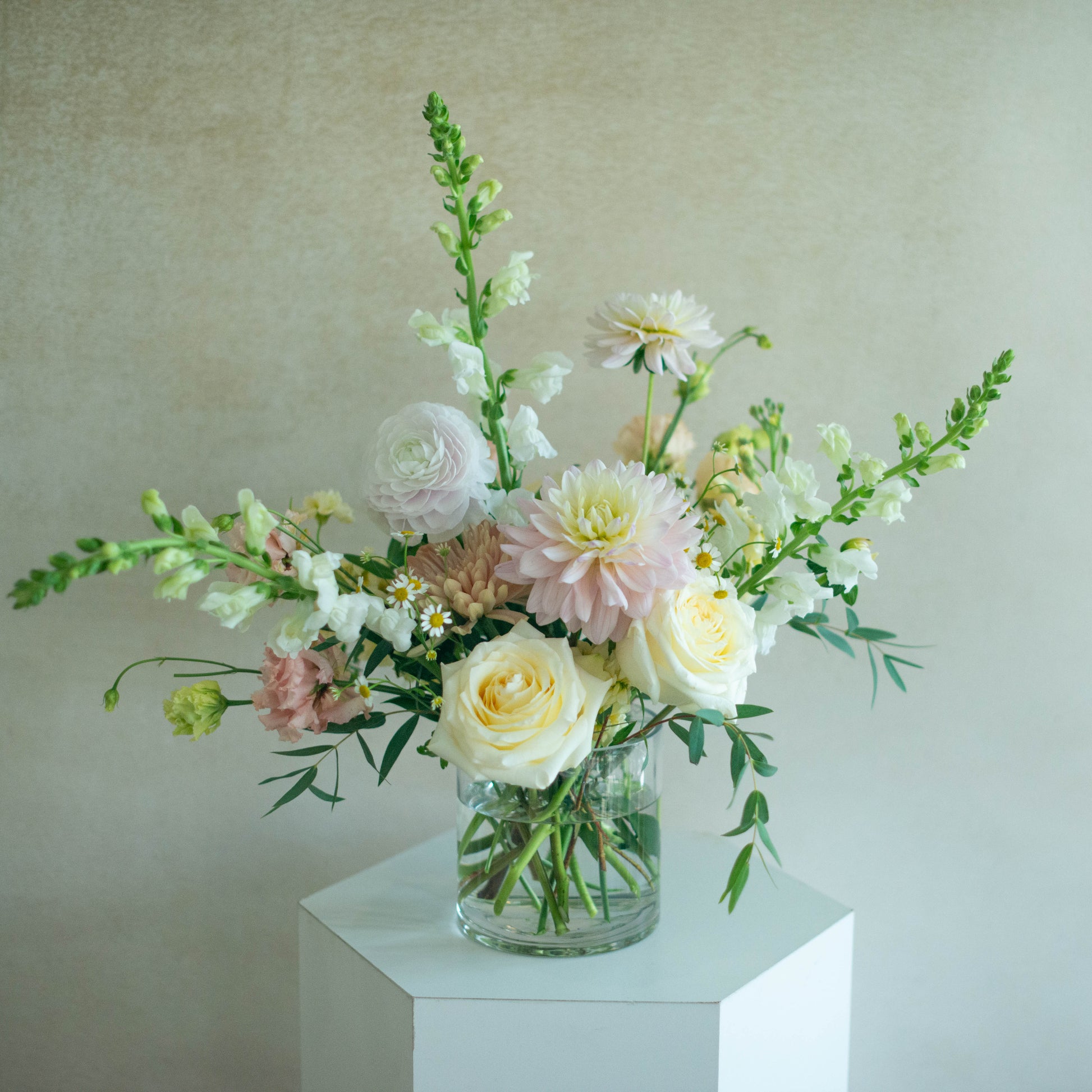 Bouquet of flowers in a clear vase on a white pedestal against a light background