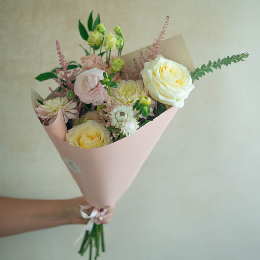 Bouquet of flowers wrapped in pink paper held by a person against a neutral background