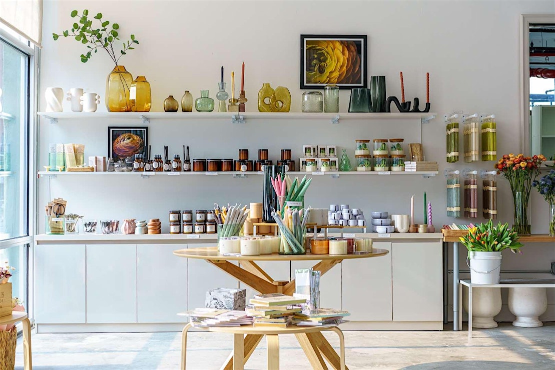 A beautifully curated display at Everwild Blooms, featuring shelves of candles, vases, and other unique gift items. The arrangement includes colorful taper candles, glass jars, and artistic decor pieces, creating an inviting retail space with natural light flooding in from large windows.