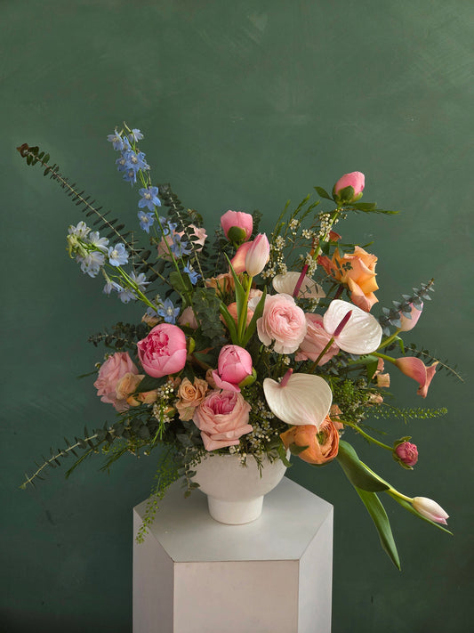 Elegant pink and peach flower arrangement in a white vase against a green background.