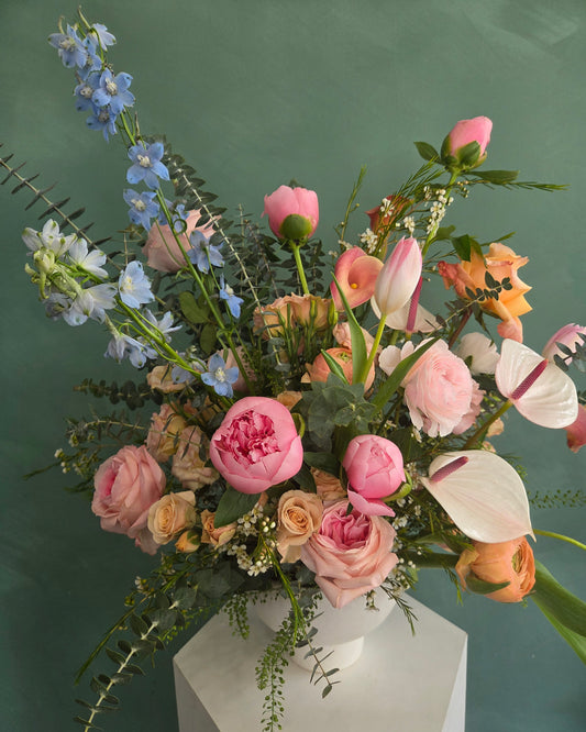 Elegant pink and peach flower arrangement in a white vase against a green background.