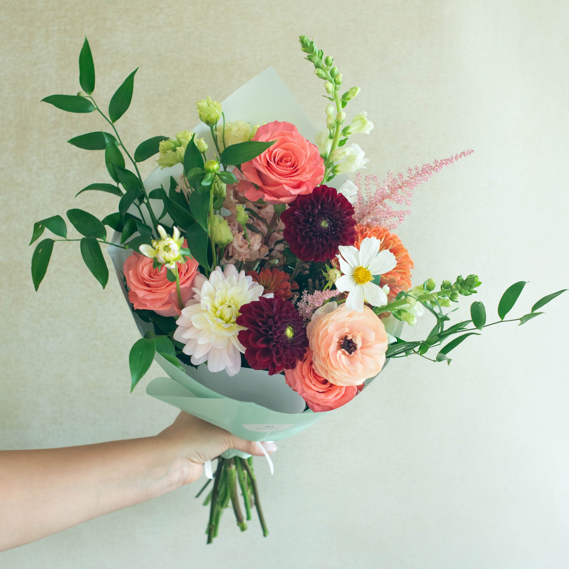 Bouquet of colorful flowers held by a hand against a light background