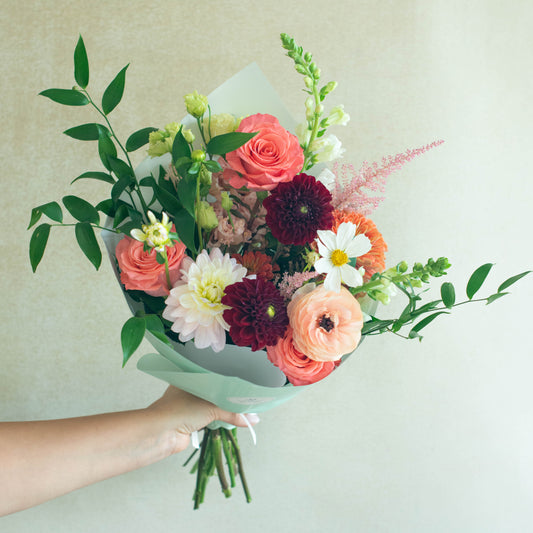 Bouquet of colorful flowers held by a hand against a light background