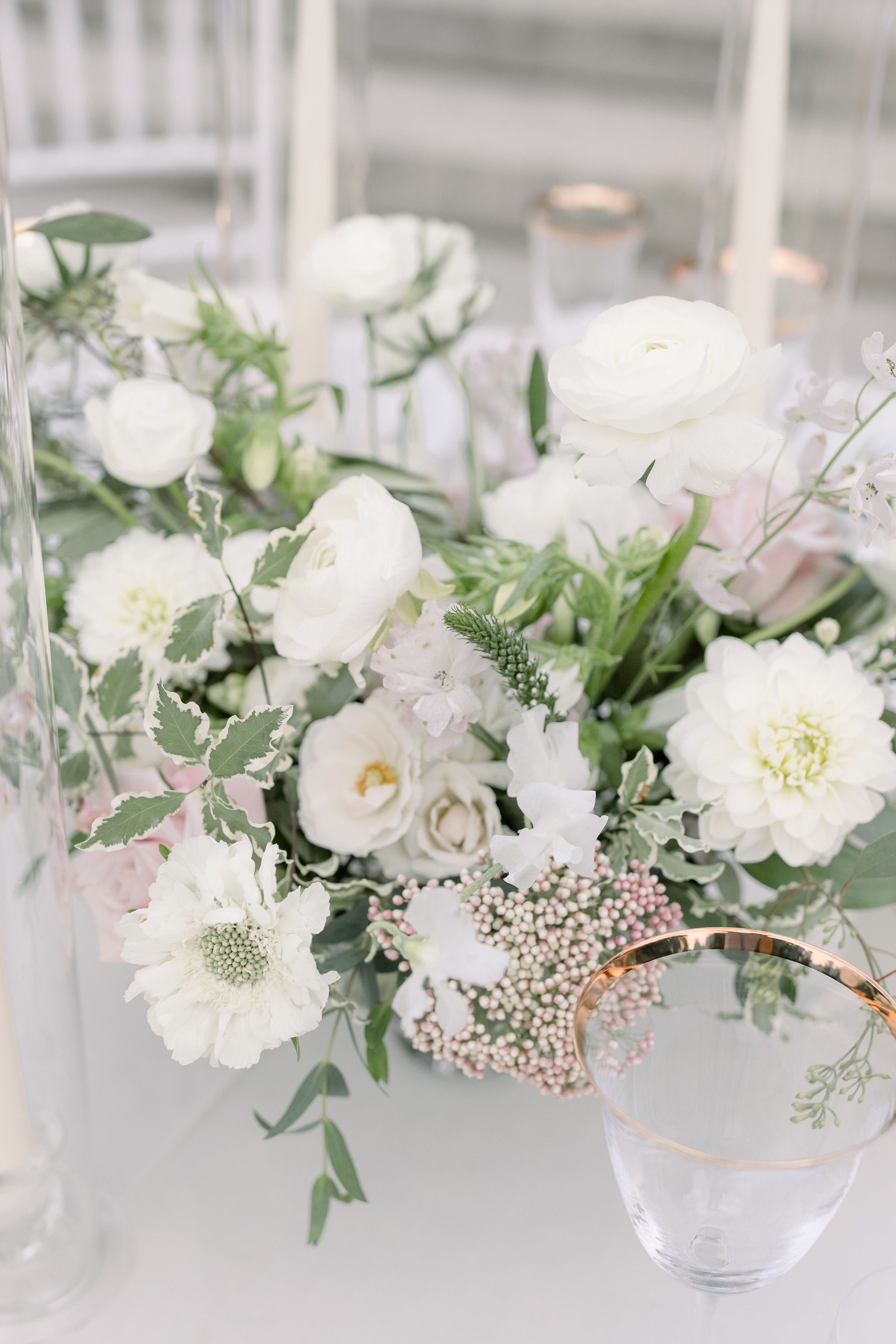 A delicate white floral centerpiece featuring ranunculus, dahlias, and soft greenery, adding an elegant touch to a wedding or event table setting.