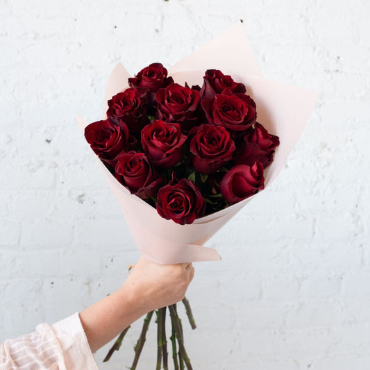 A classic bouquet of deep red roses wrapped in pale pink paper, symbolizing love and passion, perfect for romantic occasions.