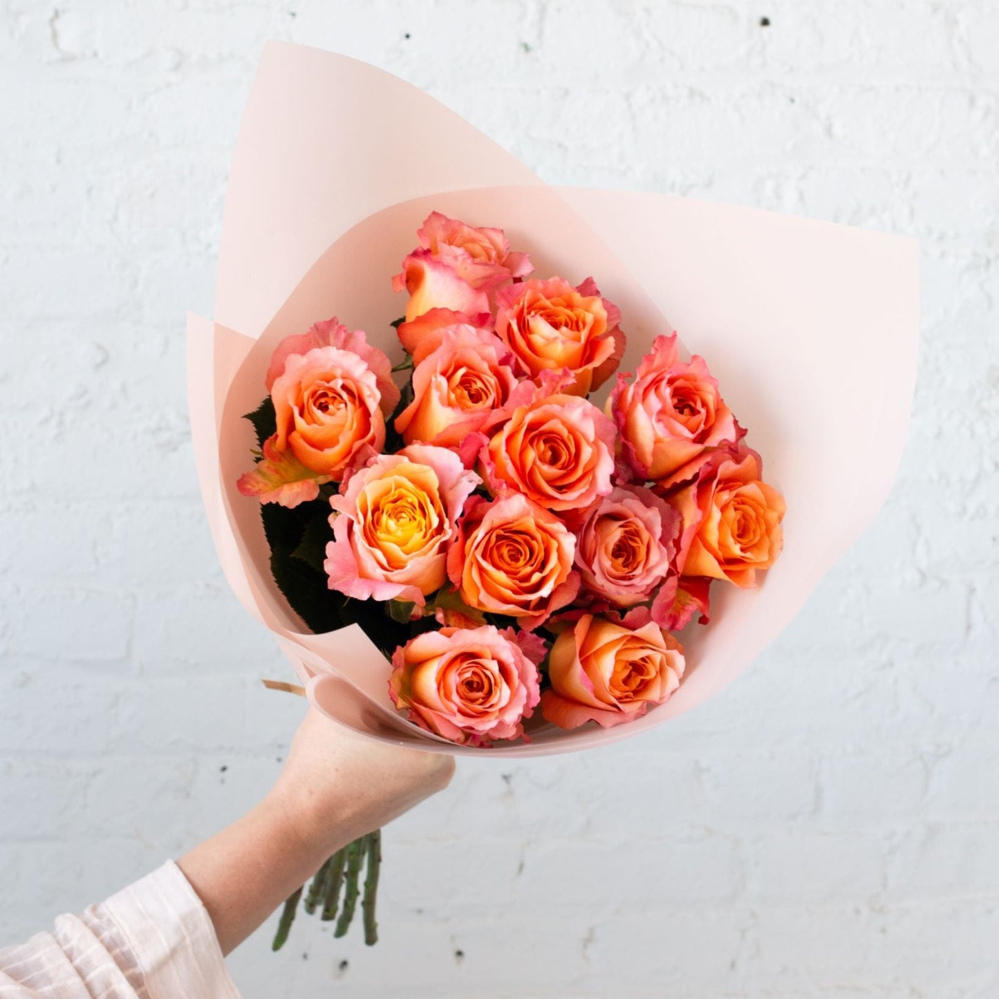 A bouquet of peach and pink roses wrapped in soft blush paper, featuring vibrant hues and delicate petals for an elegant gift.